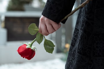 Person in schwarzem Mantel hält rote Rose in der Hand